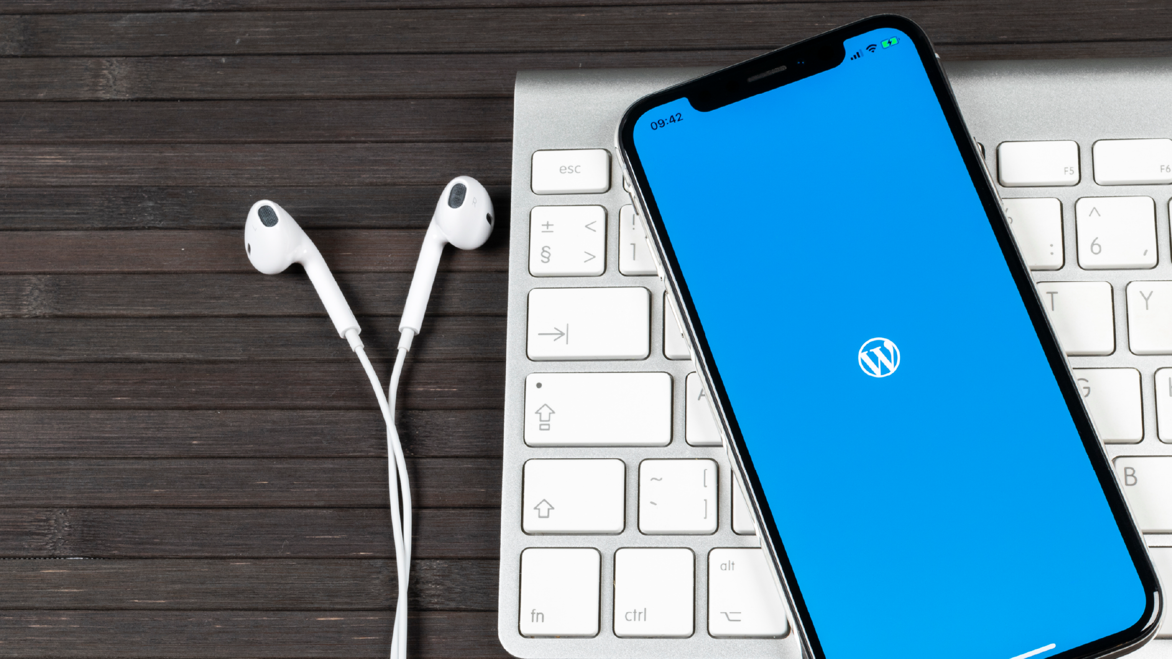WordPress on a mobile screen, resting on a Mac keyboard next to some in-ear headphones